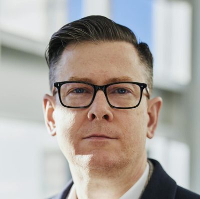 Profile portrait of a confident business executive wearing eyeglasses in a sunlit office setting.